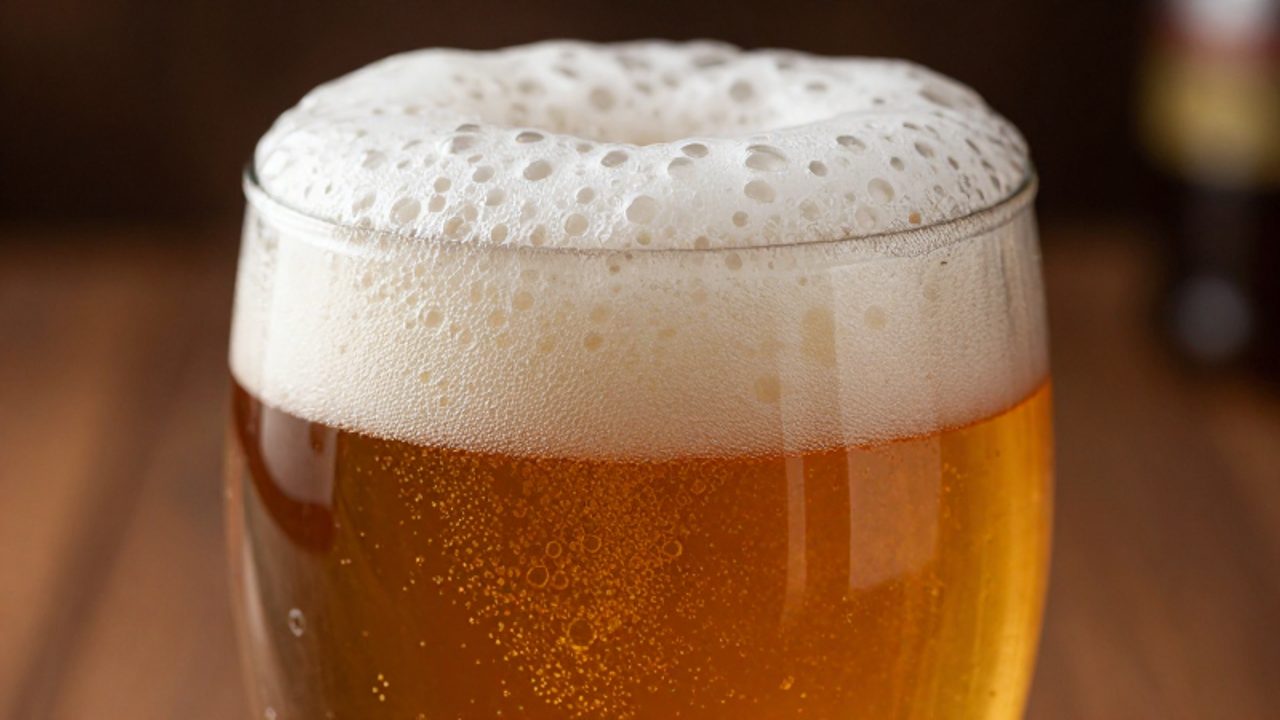 Primer plano de la textura de una espuma blanca y densa con burbujas pequeñas sobre una cerveza de color ámbar en un vaso.