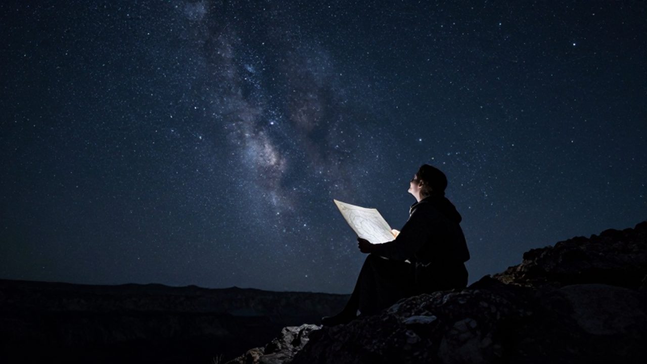 Un astrónomo antiguo observa bajo un cielo nocturno estrellado mientras sostiene un mapa de los cielos en un paisaje rocoso.