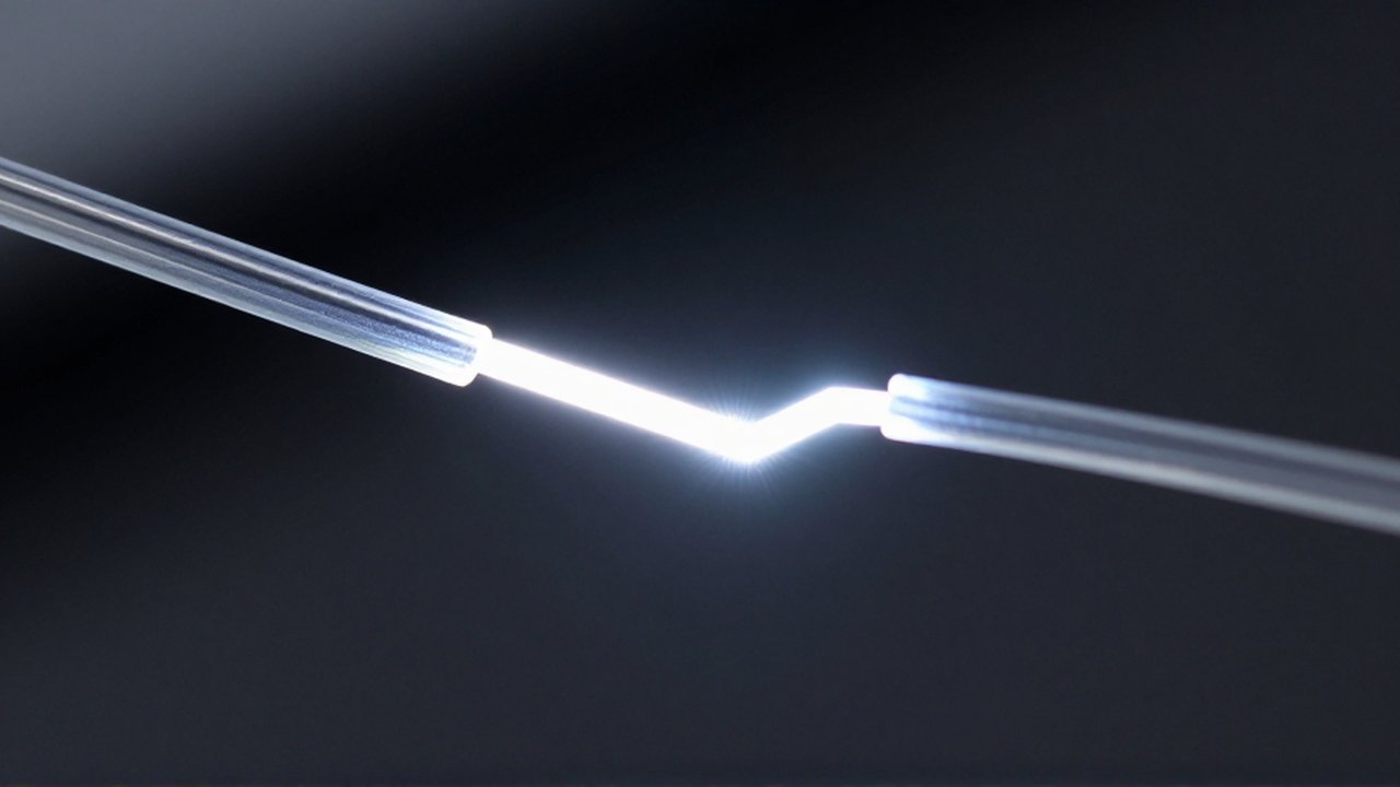 Un haz de luz brillante zigzaguea mediante reflexiones internas a través de una fibra óptica de vidrio transparente sobre un fondo oscuro.